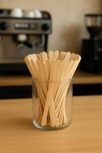 Een glazen pot gevuld met houten roerstaafjes op een horeca-toonbank, milieuvriendelijk en biologisch afbreekbaar, klaar voor gebruik bij koffie en thee.