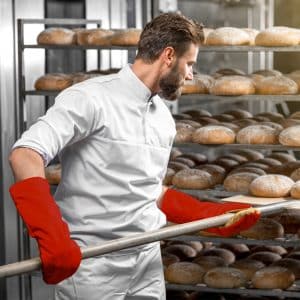 Bakker schuift broden in de oven met hittebestendige ovenhandschoenen aan