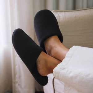 Voeten hangend over een bankleuning met luxe zwarte velours hotel slippers aan